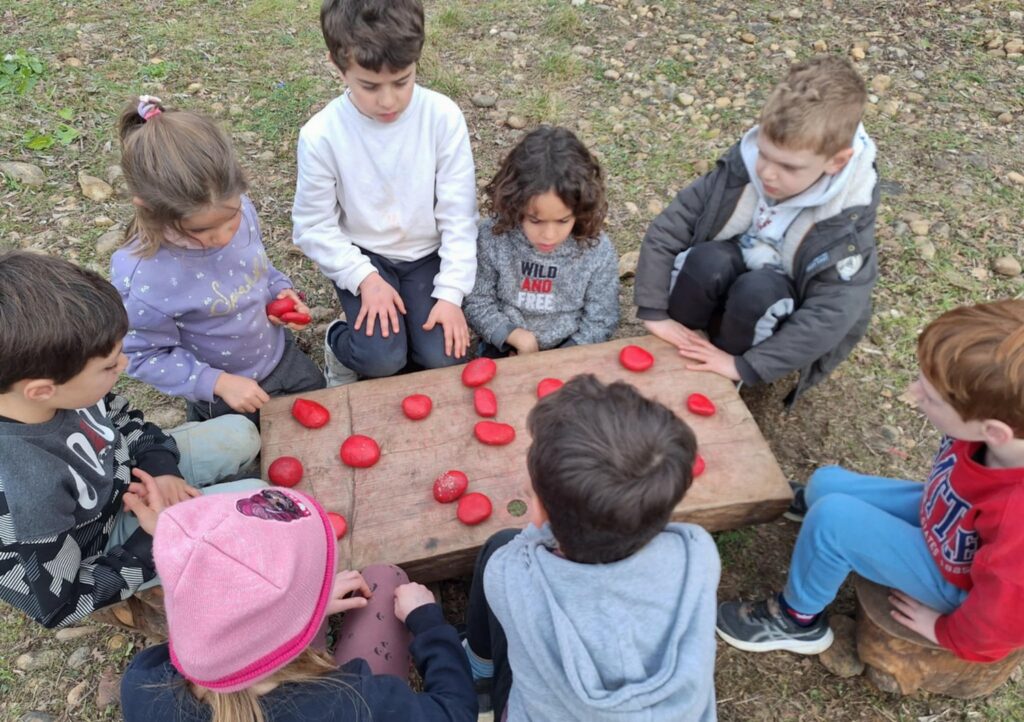 Des enfants de l'accueil de loisirs jouent avec des galets peints en rouge posés sur une table en bois.