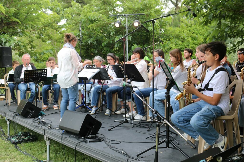 Orchestre à vent jouant sur une scène en extérieur, au milieu de la végétation.