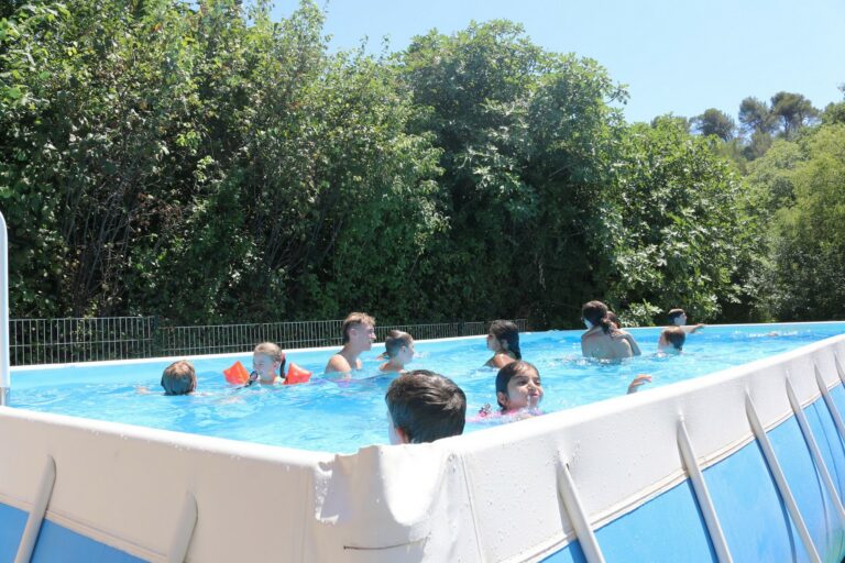 Des enfants se baignent dans la grande piscine de l'accueil de loisirs sous la surveillance d'un animateur.