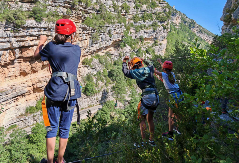 Des enfants de l'accueil de loisirs accrochés à un câble avec des mousquetons, sur. le parcours d'une via ferrata