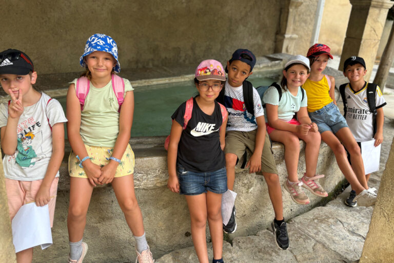 Des enfants sont assis sur le rebord d'un lavoie dans un village.