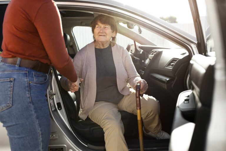 Une femme assise côté passager d'une voiture est aidée par une une autre personne pour en descendre.