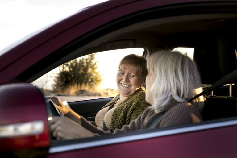 Deux femmes souriantes discutent à l'avant d'une voiture.