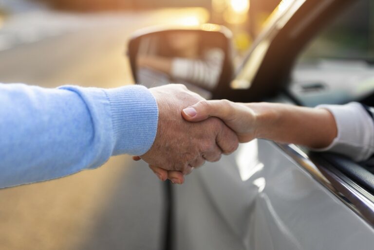 Echange d'une poignée de main à travers la vitre d'une voiture côté conducteur.