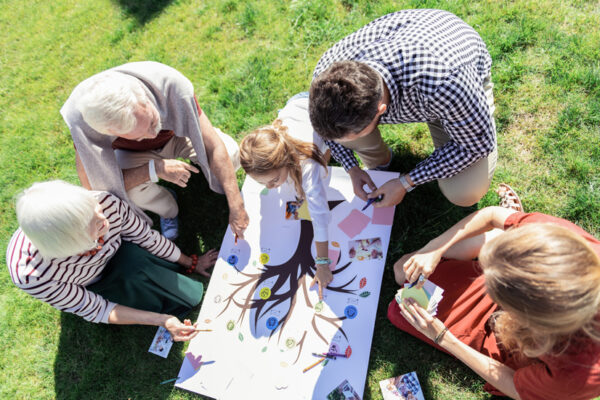 Une famille installée dans un jardin réalise un arbre généalogique sur une grande feuille.