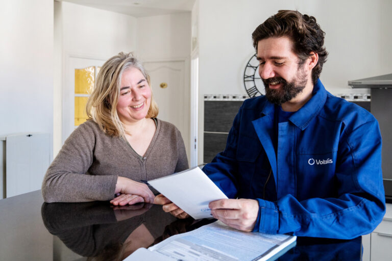 Un technicien de la société Voltalis discute avec une cliente autour d'une table.
