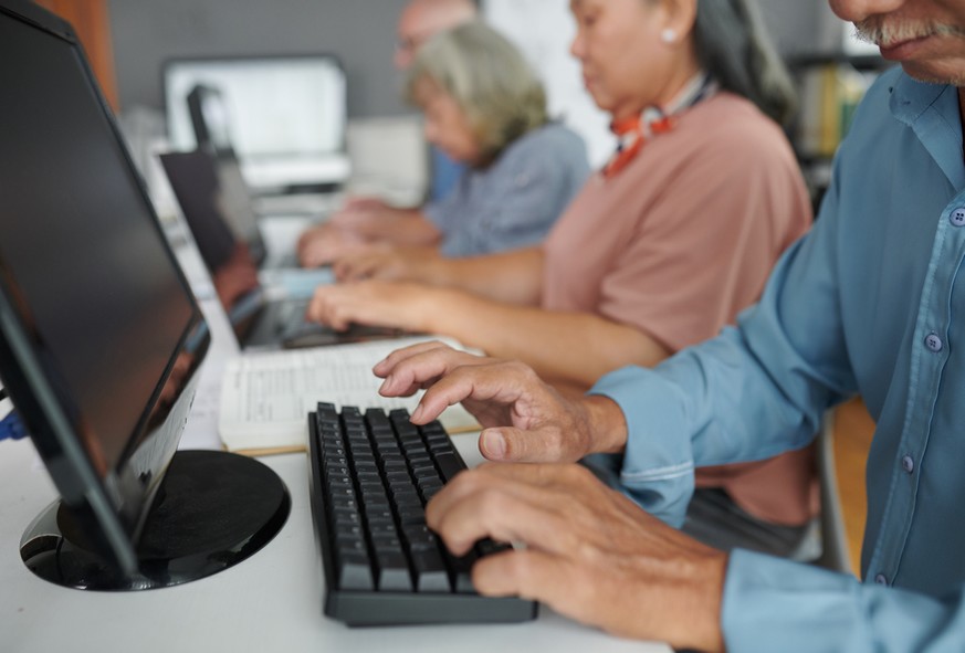 Des personnes s'initient à l'informatique devant des ordinateurs.