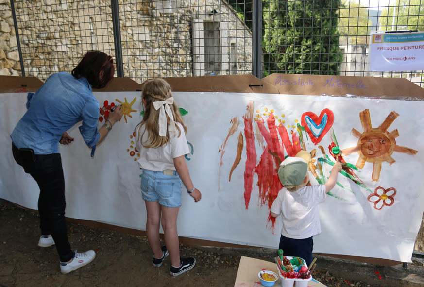 Une femme et deux enfants peignent sur une grande affiche murale.