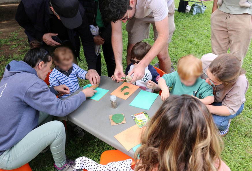 Des enfants et leurs parents sont autour d'une table basse en extérieur. ils participent à un atelier créatif.