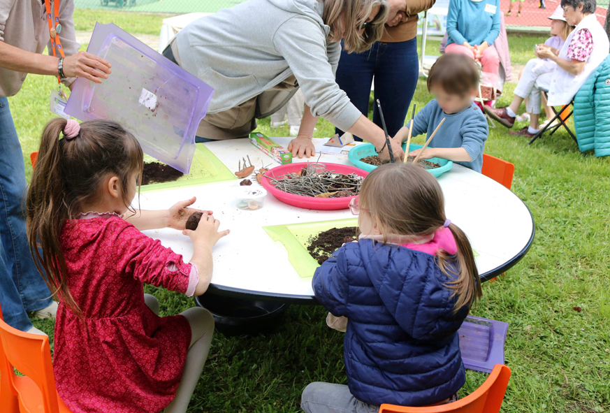En extérieur, des enfants autour d'une table basse participent à un atelier créatif.