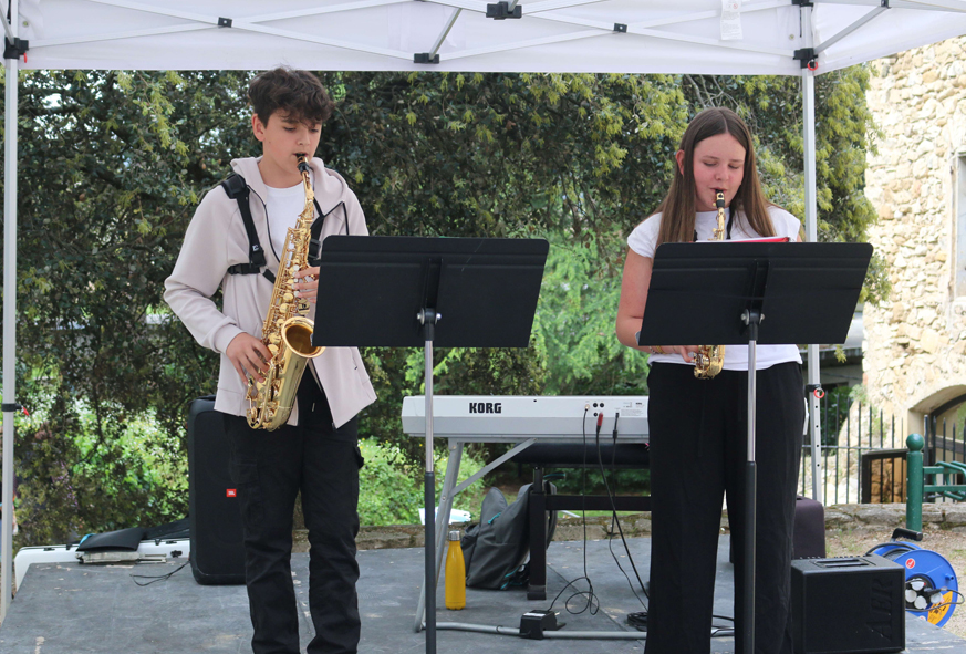 Deux adolescents jouent du saxophone sur une petite scène installée en extérieur.