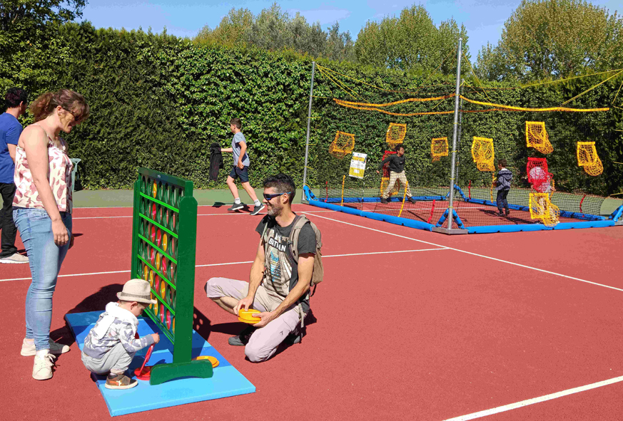 Des parents et des enfants jouent avec des jeux géants installés sur un court de tennis.