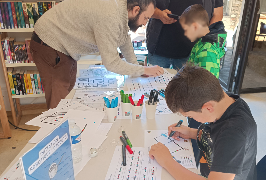Un homme explique à des enfants comment réaliser un atelier de programmation informatique simple avec un mini-robot.
