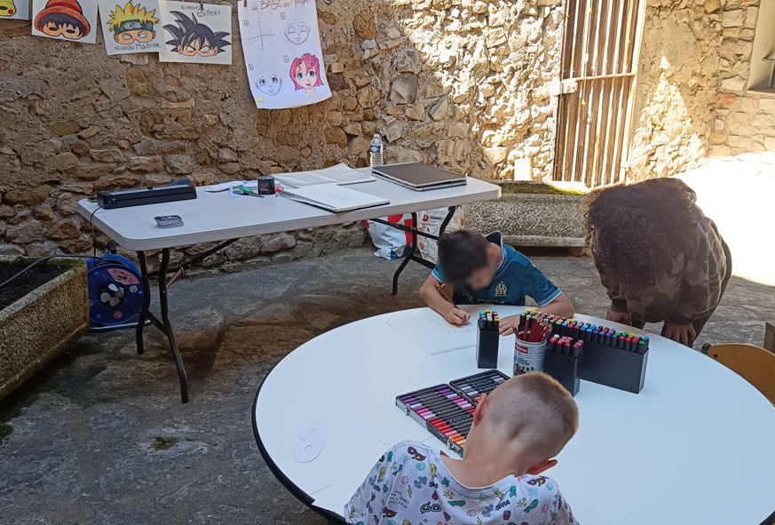 Dans une petite cours de la Ferme des arts à Vaison-la-Romaine, deux enfants et une adulte participent à un atelier créatif pour fabriquer un masque à l'effigie de son avatar manga.