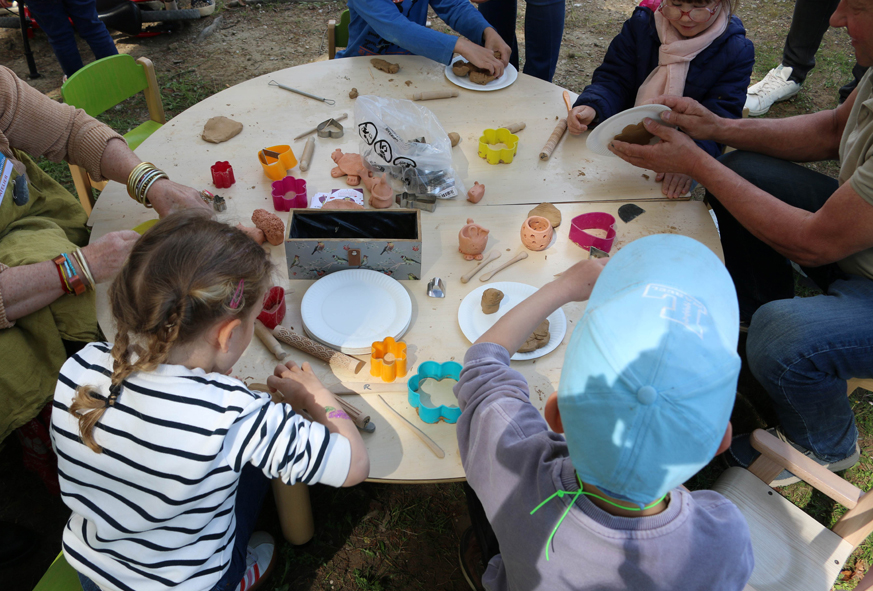 Des enfants de dos, assis autour d'une table basse ronde, participent à un atelier créatif de poterie.