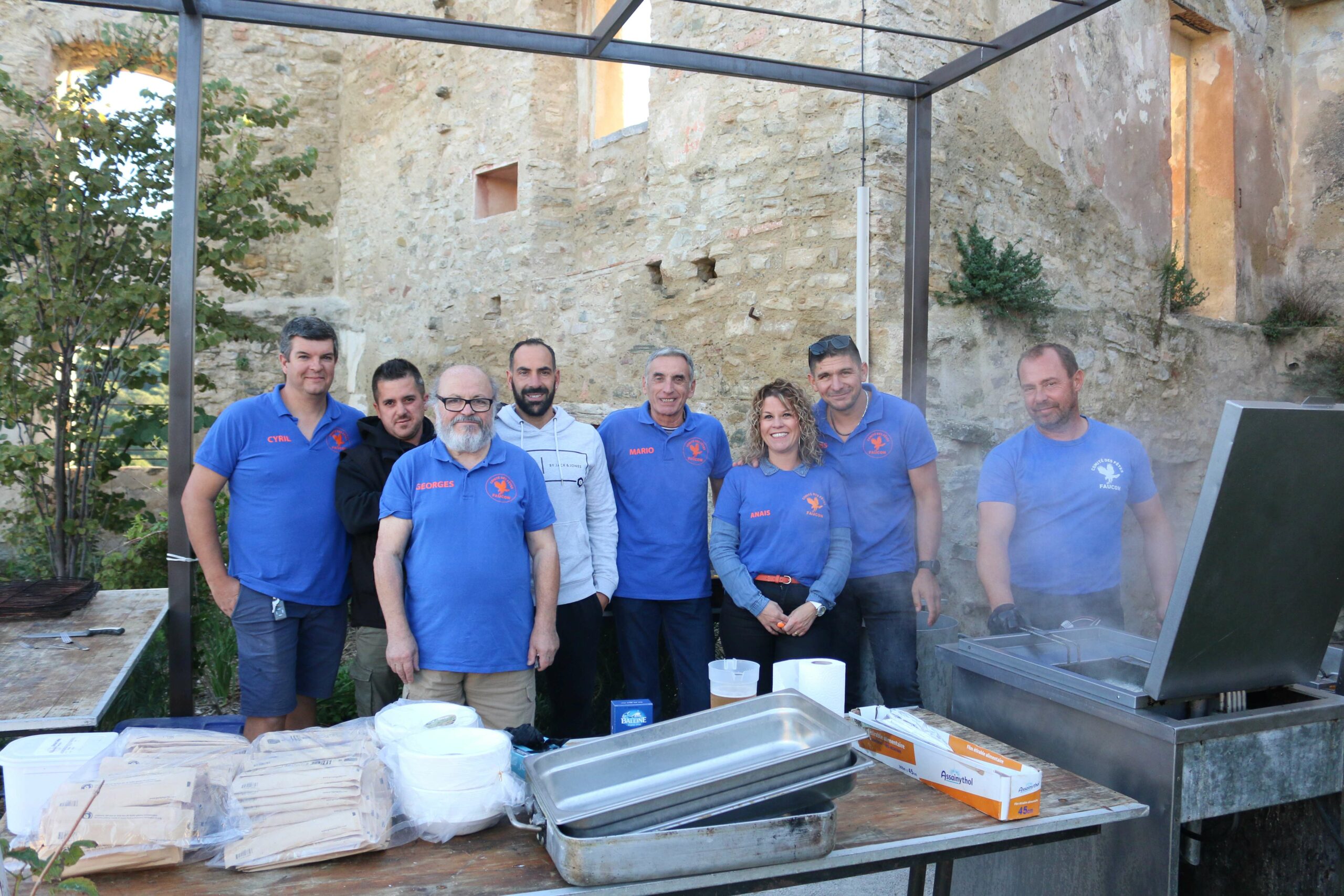 Huit membres de l'équipe du Comité des fêtes de Faucon posent sur le stand de préparation du repas des Automnales 2025.