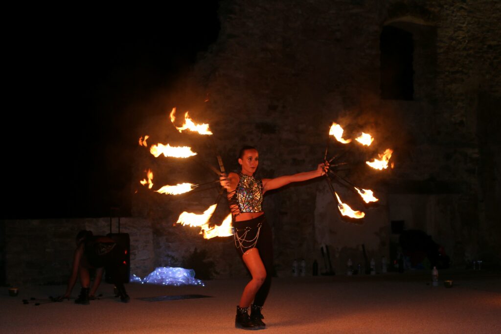 Une femme danse, de nuit, avec des baguettes enflammées.