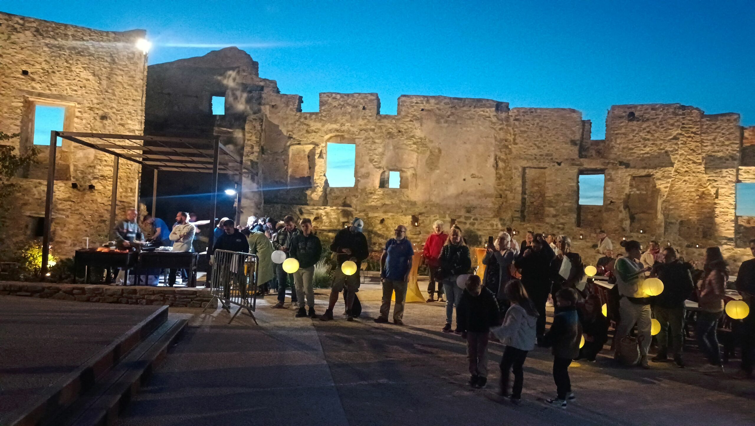 La place des remparts de Faucon (place du 30 mai 1565) illuminée à l'occasion des Automnales 2025 avec le public portant des lampions.